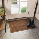 A medium-sized, brown all-weather doormat with a crisscrossing linear pattern, placed inside a single door on stone tile flooring; a pair of clean, black boots are sitting on top. 