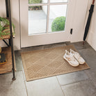 A medium-sized, light golden-colored WaterHog doormat with a diamond pattern, is inside a single door on tile flooring with a pair of clean, white sneakers placed on top.