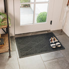 A 2x3, dark grey/black all-weather WaterHog doormat with a linear crisscrossing design, placed inside a single door, on tile flooring, with a pair of black and white striped flats sitting on it. 