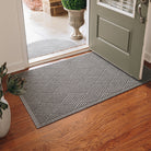 A large-sized, medium grey WaterHog doormat with a crisscrossing, linear design placed inside a single door on wood flooring, with the door open. 