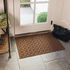 A medium-sized, brown WaterHog doormat, with a repeating dog bone pattern, is placed on tile flooring inside a single door with a black bag sitting off to the side. 