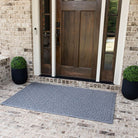 A large bi-level doormat in a light blue/grey color with an interlocking elliptical pattern is on brick flooring placed outside of a single door with sidelights. 