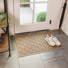 
A medium-sized, light golden WaterHog doormat with a interlocking elliptical pattern is placed on tile flooring inside a single door with a pair of white sneakers sitting on top. 