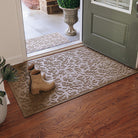 An entrance way with two WaterHog Fall Day Mats with a fallen leaves design in a tan color. A large 3x5 mat is placed inside with boots on top of it, while a 2x3 version is placed outside.