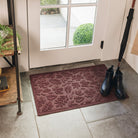 WaterHog Doormat in a maroon color with a scattered leaf pattern placed inside a doorway with boots on the mat.