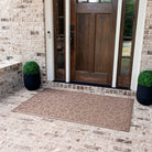 An extra large, 4x6, camel doormat with a bi-level fallen leaves design placed outside in front of a single door.