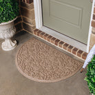 A half round WaterHog front doormat in a camel color with a fallen leaf design placed in front of a single door.