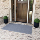 A large WaterHog Squares doormat on a white-washed brick porch, made with a bi-level design for dirt and moisture trapping.