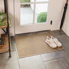 A medium, camel colored WaterHog Squares doormat placed at a side door entrance with a pair of sneakers on top.