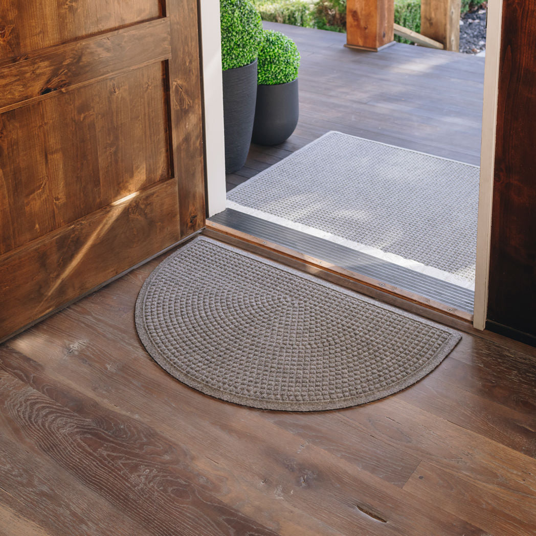 Dreamy image of a pair of WaterHog Squares doormats, a large doormat and a half round doormat, at the front door of a house stopping the tracking of mud and moisture.