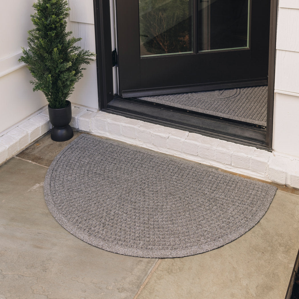 An all-weather WaterHog Squares half-round doormat placed outside a side door on a stone walkway for floor protection from outdoor elements.