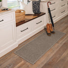 A cozy mudroom or entryway protected by a medium gray WaterHog runner mat with a bi-level square pattern on a light wood floor and a pair of duck brown boots placed on top.