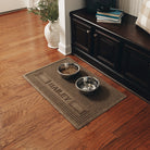 A large WaterHog Squares pet mat personalized with the name Bailey in all caps on a brown mat, with a water and food dish on top while the mat protects the hardwood floors from spills and messes.