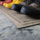 Close up image of low-profile WaterHog Squares boot tray mat with three pairs of boots sitting on top. 