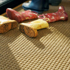 Close up of WaterHog Squares doormat in the color camel with kids muddy boots laying on top for floor protection.