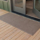 A WaterHog Honeycomb Runner mat at the front door of a green cabin house