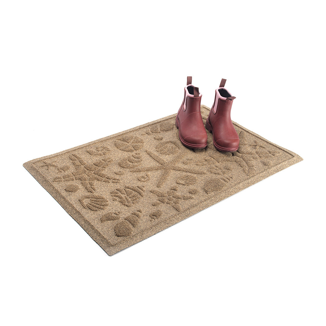 A pair light red rain boots placed on top of a Medium WaterHog Beachcomber all-weather doormat.