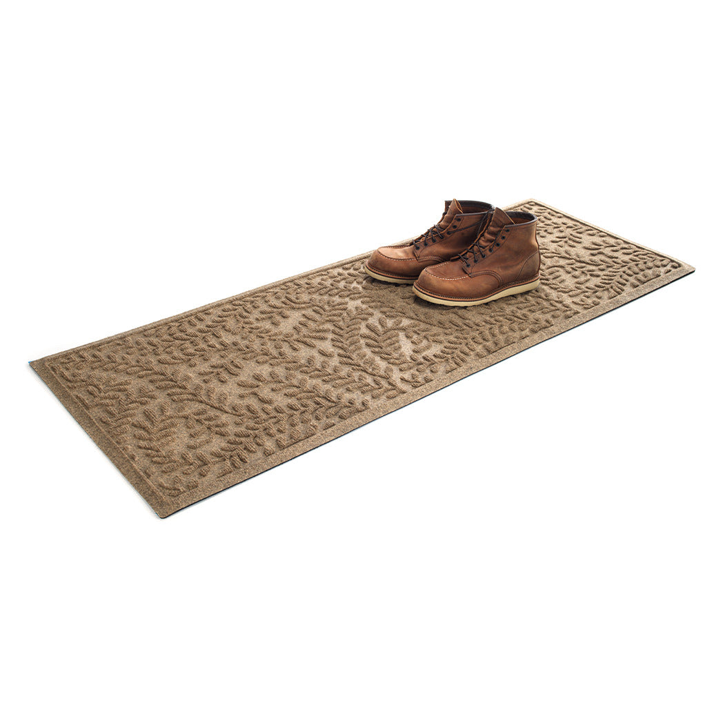 Isolated WaterHog 2x5 runner mat shown in camel with a pair of men's boots on top on a white background.