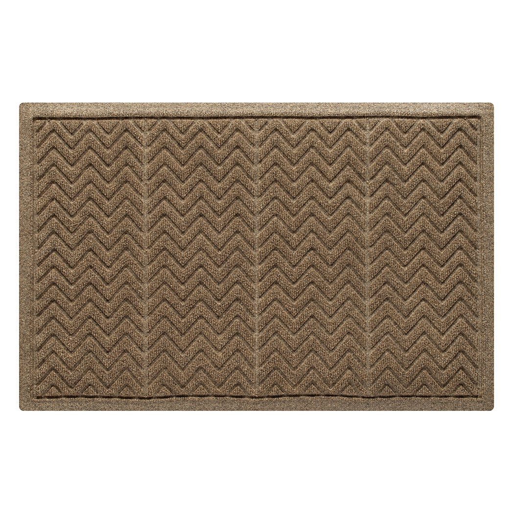 This image features a rectangular WaterHog doormat in a neutral brown or tan color. The mat has a distinct zigzag or chevron pattern, divided into vertical sections, designed to effectively scrape dirt and absorb moisture. It is surrounded by a reinforced border, which helps contain water and debris, preventing spills onto surrounding floors. The textured surface is made from recycled synthetic fibers with a rubber backing, making it suitable for high-traffic areas.