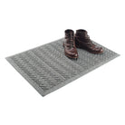 Modern WaterHog indoor/outdoor doormat in a medium grey color with a zig-zag v-shaped pattern with a pair of brown leather boots placed on top. 