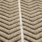 close-up of a textured mat with a bold chevron pattern. Made from a durable, recycled materials in a neutral brown or tan color. The raised sections are designed for effective dirt and moisture trapping, making it suitable for entryways or high-traffic areas.