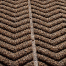 Close-up of a textured WaterHog doormat with a bold herringbone or chevron pattern made from a fibrous material consisting of cclors brown, black, and grey. The raised sections of the pattern create a three-dimensional effect designed for effective dirt and moisture trapping. 