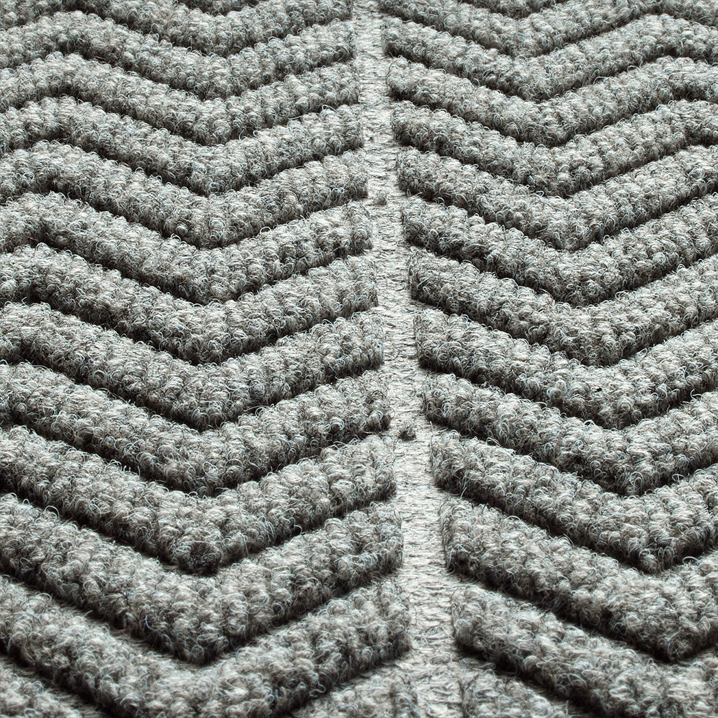 Close-up of a textured WaterHog doormat with a  chevron pattern made from a fibrous material consisting of colors light grey and dark grey. The raised sections of the pattern create a three-dimensional effect designed for effective dirt and moisture trapping. 