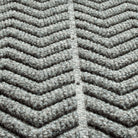 Close-up of a textured WaterHog doormat with a  chevron pattern made from a fibrous material consisting of colors light grey and dark grey. The raised sections of the pattern create a three-dimensional effect designed for effective dirt and moisture trapping. 