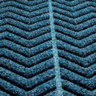 close-up of a WaterHog doormat with a chevron pattern. Made from a durable, recycled materials. The color scheme is predominantly deep blue with lighter blue highlights, giving it a rich, textured appearance. The raised sections of the pattern create a three-dimensional effect, suggesting that the mat is designed for effective dirt and moisture trapping, making it suitable for entryways or high-traffic areas.