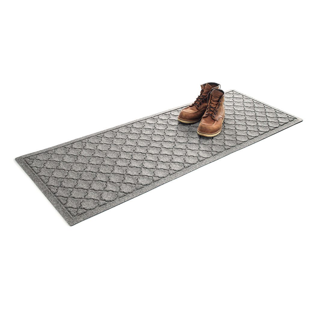 Isolated WaterHog 2x5 runner mat shown in a light grey with a pair of men's boots on top on a white background.