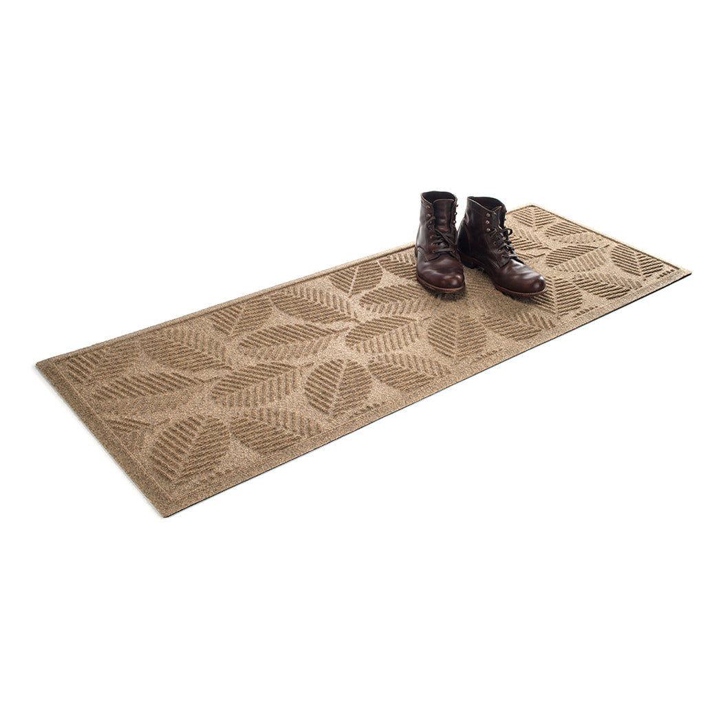 A luxury WaterHog 2x5 outdoor runner mat in camel with a set of clean boots resting on top  on a white background.