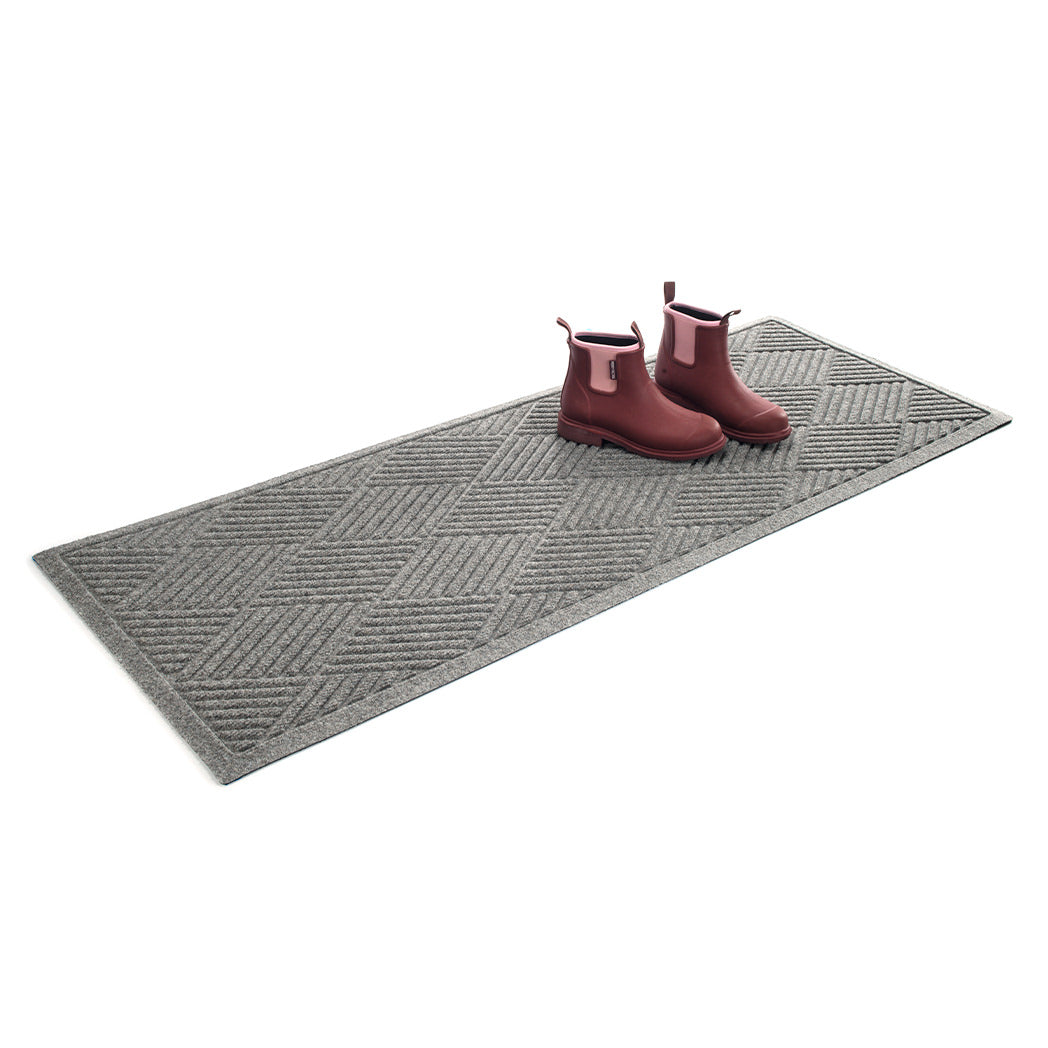 Isolated WaterHog 2x5 runner mat shown in a light grey with a pair of men's boots on top on a white background.