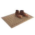 Isolated Angle of WaterHog 2x3 Dog Bones doormat in traditional camel color with a pair of brown leather boots placed on top.