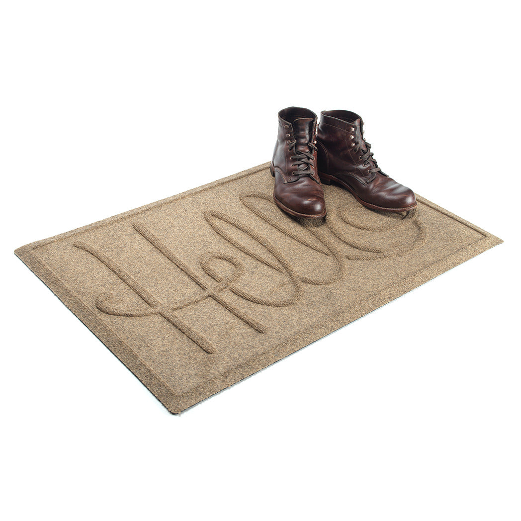 A WaterHog Hello door mat in a tan color with an elevated design that spells hello and boots placed on top of the mat.