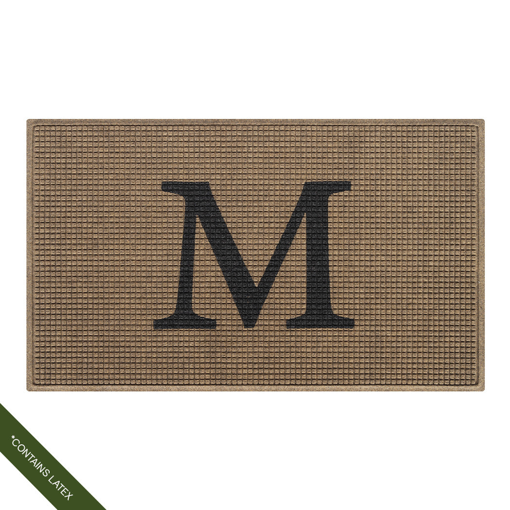The original WaterHog Squares doormat in a large size shown in camel monogrammed with a serif capital 'W' in charcoal in the center; latex disclaimer