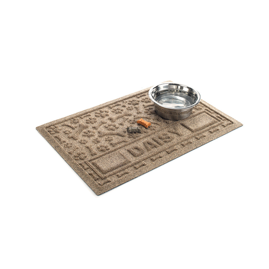 Angled WaterHog Paws & Bones personalized bowl mat in medium grey with a water bowl and dog treats on top.