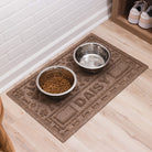 A WaterHog Paws & Bones bowl mat personalized with the name Daisy holding dog dished on a fast drying, easy-cleaning pet mat.