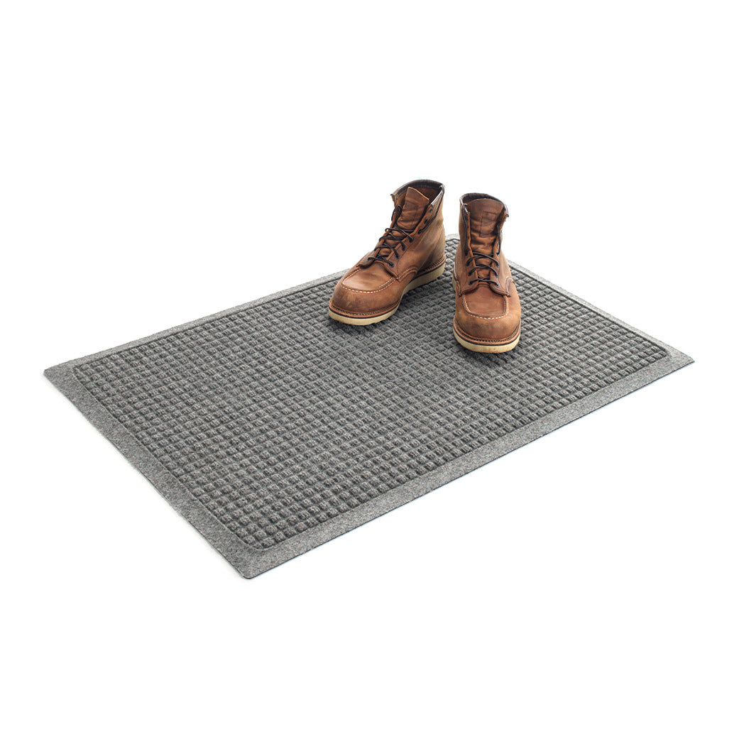 Isolated, angled image of a 2x3 WaterHog doormat shown in a medium grey with a pair of brown leather boots placed on top.