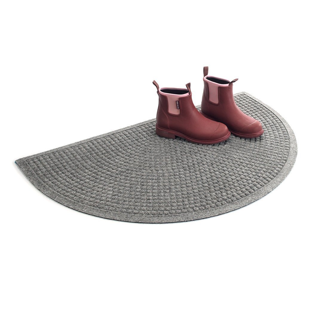 Isolated WaterHog Squares half-round doormat in a medium grey with a pair of pink rubber boots on top.