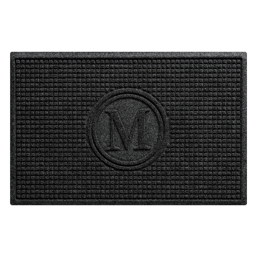 WaterHog Squares modern doormat is monogrammed with the letter M encased in a circle, surrounded by a uniform square grid design, shown in the dark, deep grey.