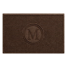 An above shot of a WaterHog Squares modern doormat, monogrammed with the letter M encased in a circle, surrounded by a uniform square grid design, shown in a dark, deep grey.