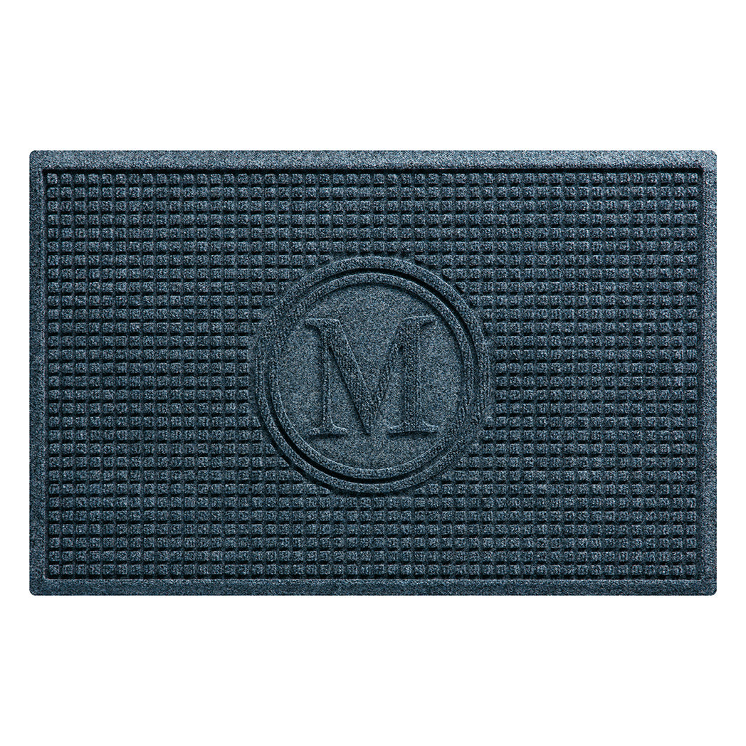 Overhead of a WaterHog Squares outdoor doormat monogrammed with a serif M, encased by two circles surrounded by a uniform grid design in a relaxed blue color; an American-made mat.
