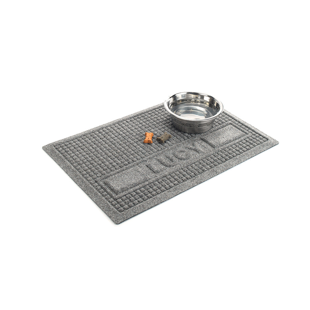 Angled WaterHog medium Squares personalized bowl mat in medium grey with a water bowl and dog treats for size reference.