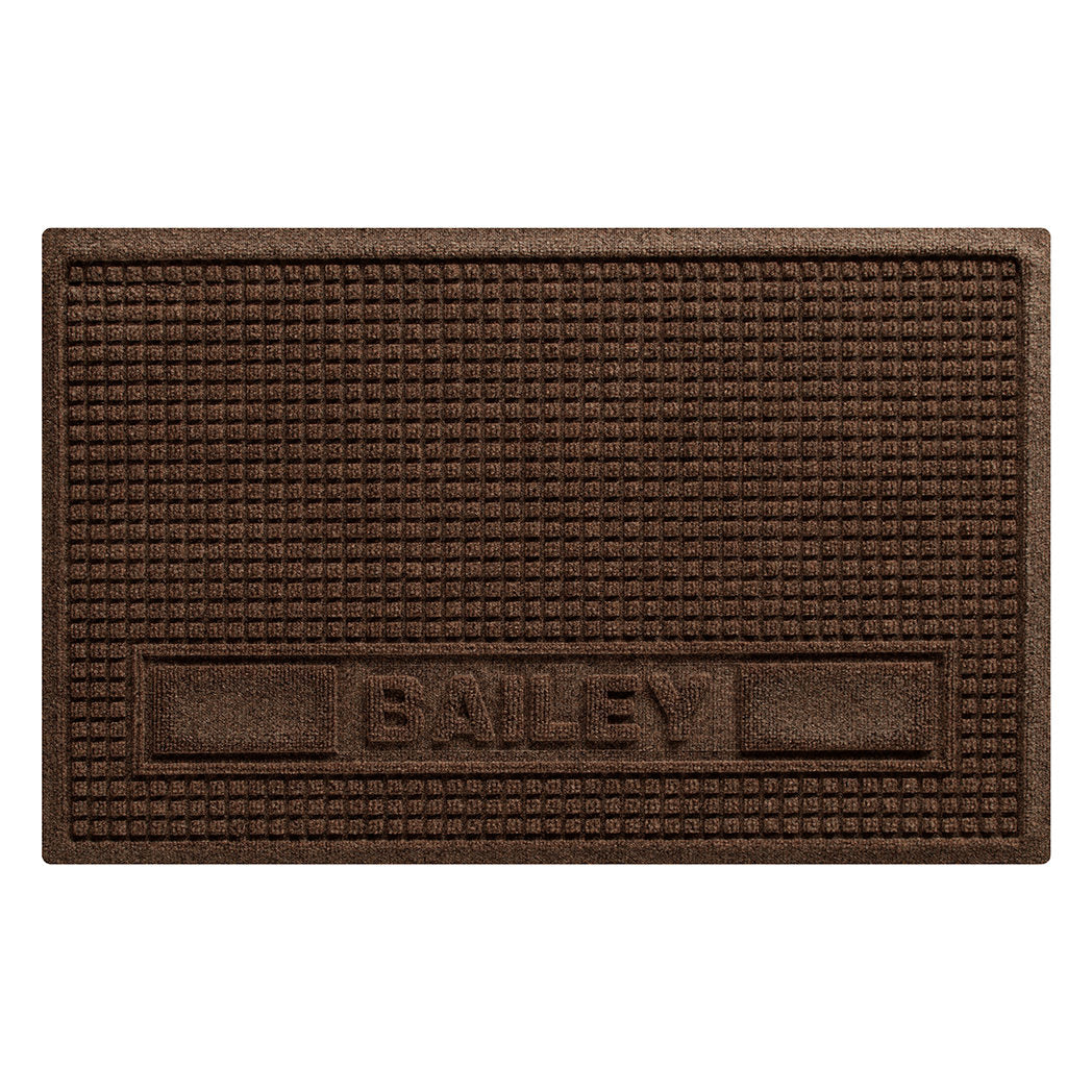 Overhead of a large WaterHog Sqaures pet mat personalized with the name Bailey in all caps in the lower center of the mat, with two medium rectangular blocks on the side, in a dark earthy brown surface.