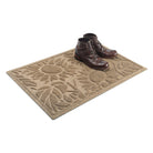 A pair of dark brown leather boots sitting on the far right side of a WaterHog Sunshine Day 2x3 doormat in the color camel, shown on a white background.