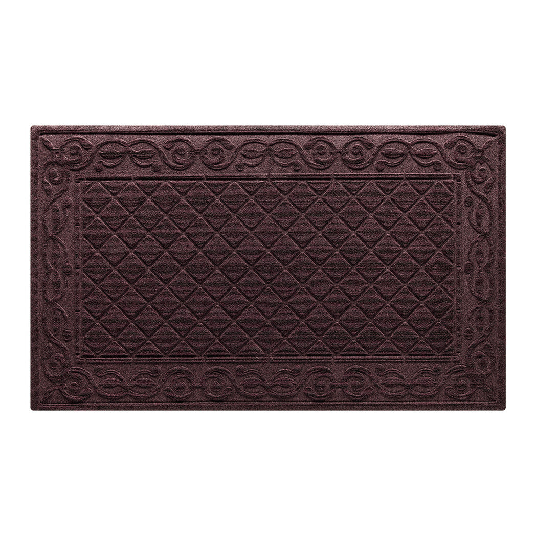 An overhead view of a large, dusty red Tristan all-weather doormat, which features an ornate scrollwork pattern that borders the classic, squared-off diamonds pattern in the center; all in a bi-level design and with a water dam border.