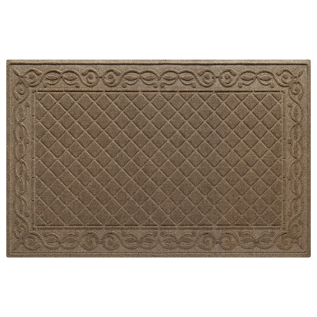 An XL WaterHog Tristan doormat in tan with a two-part bi-level design for scraping and trapping messes - a diamond pattern that is surrendered by an ornate scroll design.