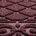 Close-up of WaterHog Tristan's doormat surface in a muted wine-red color, featuring raised diamond-shaped patterns and intricate scrollwork. The surface is made of densely woven fibers designed for durability and effective dirt trapping.