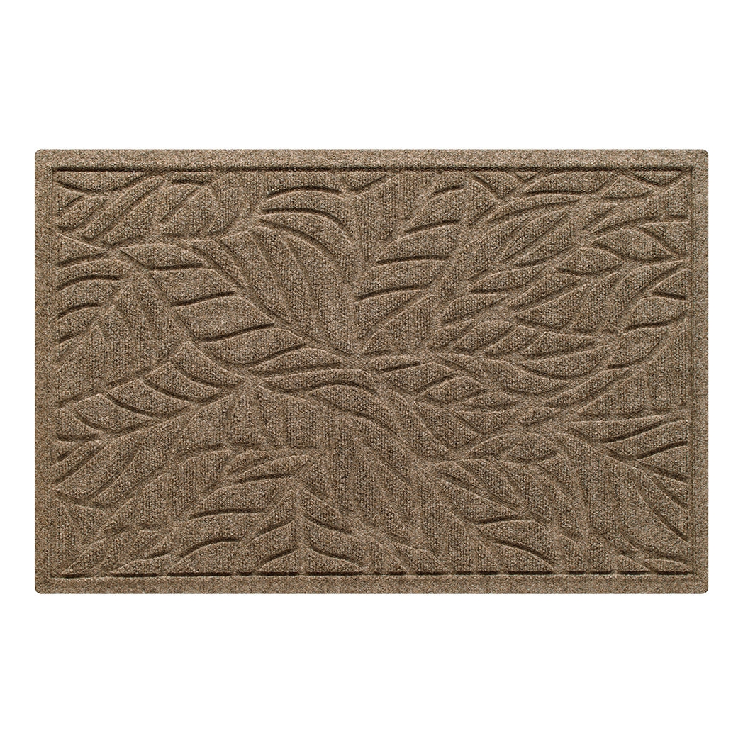 A medium WaterHog doormat in a warm camel color featuring a raised tropical leaf pattern designed to trap dirt and moisture while the bordered edges provide a clean, finished look.